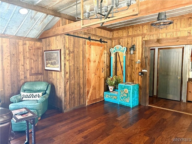 interior space with lofted ceiling with beams, a barn door, wooden walls, and wood finished floors