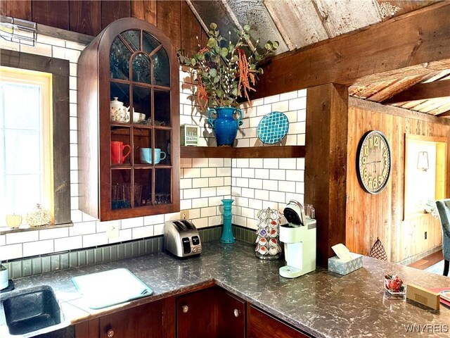 kitchen with a sink, backsplash, beamed ceiling, wood walls, and open shelves