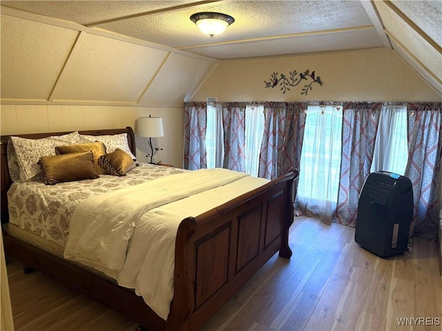 bedroom featuring a textured ceiling, light wood-style floors, and vaulted ceiling