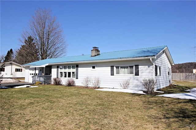 ranch-style house featuring metal roof, a chimney, a front lawn, and fence