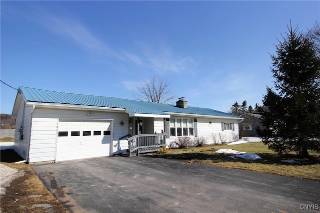 ranch-style house with a chimney, an attached garage, metal roof, and driveway