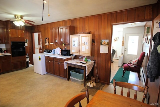 kitchen featuring wood walls, light countertops, washer / clothes dryer, black appliances, and a ceiling fan