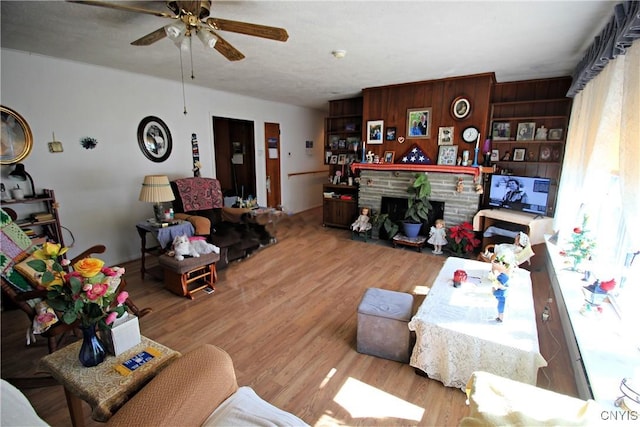 living room featuring a ceiling fan, a fireplace with flush hearth, and wood finished floors