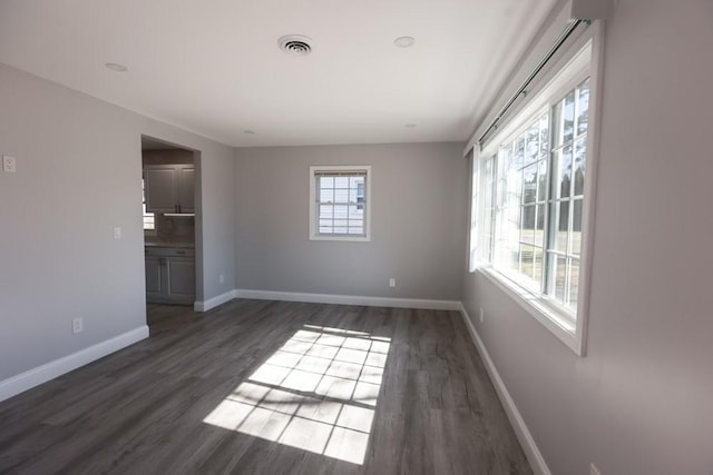 spare room with a wealth of natural light, visible vents, baseboards, and wood finished floors