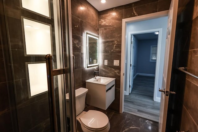 bathroom featuring toilet, tile walls, a shower stall, baseboards, and vanity