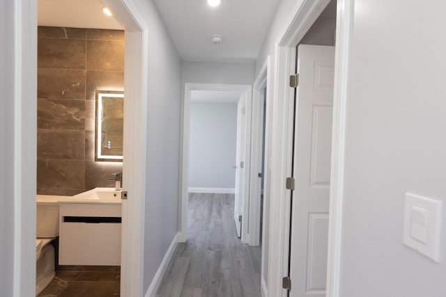 hall featuring a sink, baseboards, and wood finished floors