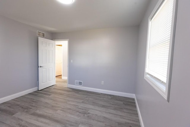 empty room featuring wood finished floors, baseboards, and visible vents