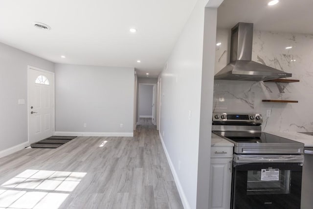 kitchen with tasteful backsplash, stainless steel electric stove, light wood-style floors, wall chimney range hood, and baseboards