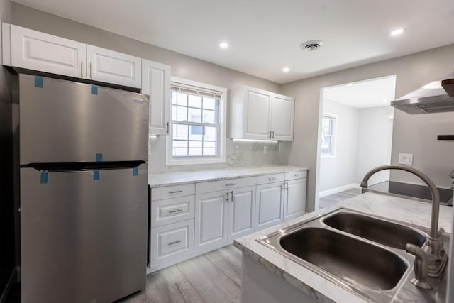 kitchen featuring visible vents, light wood-style flooring, freestanding refrigerator, a sink, and white cabinets