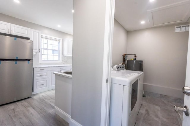 washroom featuring visible vents, light wood-type flooring, washer and dryer, water heater, and laundry area