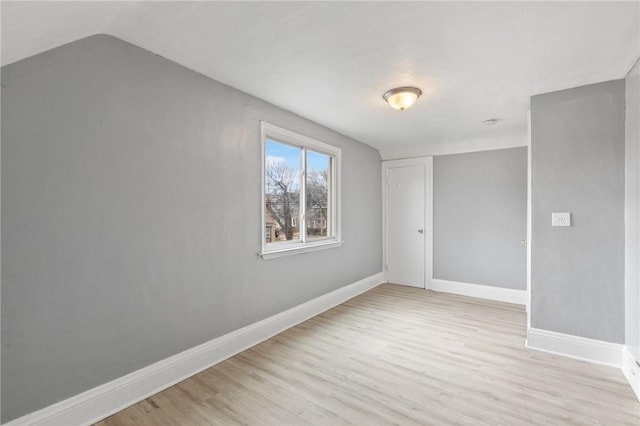 unfurnished bedroom featuring vaulted ceiling, light wood-style floors, baseboards, and a closet