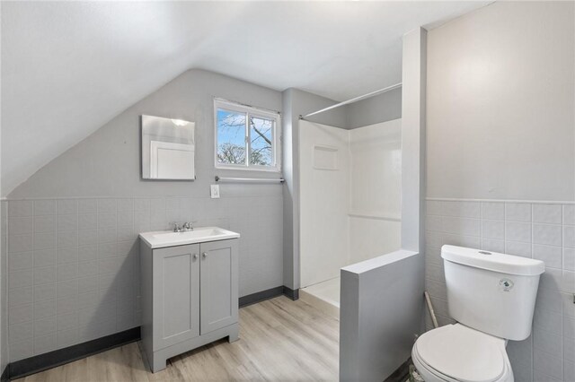 bathroom featuring wood finished floors, vaulted ceiling, a shower, tile walls, and toilet