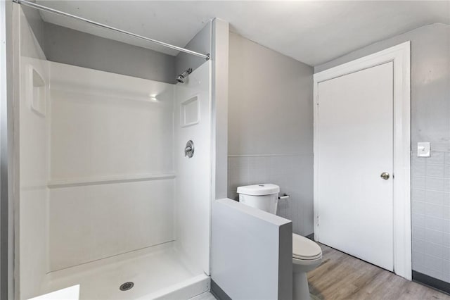 full bathroom featuring a shower stall, toilet, wainscoting, wood finished floors, and tile walls