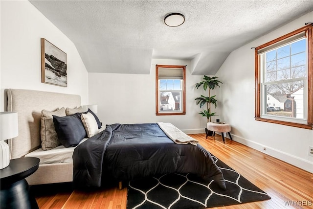 bedroom featuring a textured ceiling, baseboards, lofted ceiling, and wood finished floors