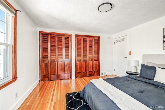 bedroom featuring baseboards, visible vents, a textured ceiling, light wood-type flooring, and two closets