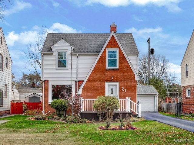 tudor house featuring fence, roof with shingles, an outdoor structure, brick siding, and a chimney