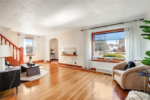 living area featuring arched walkways, a textured ceiling, stairs, and hardwood / wood-style flooring