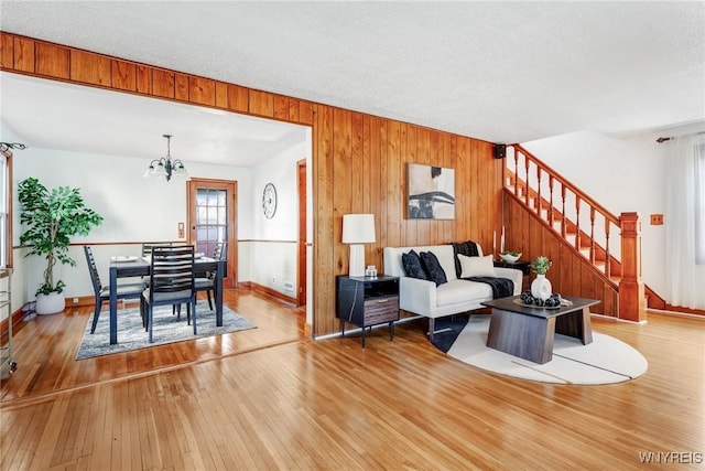 living room with stairway, wood-type flooring, a notable chandelier, and wooden walls