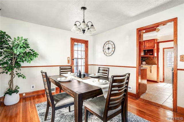 dining area with a notable chandelier, a textured ceiling, and light wood-type flooring