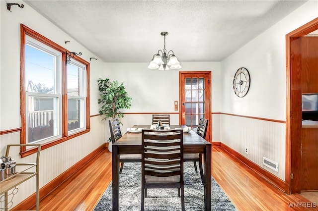 dining area with light wood-type flooring, visible vents, a textured ceiling, and a wainscoted wall