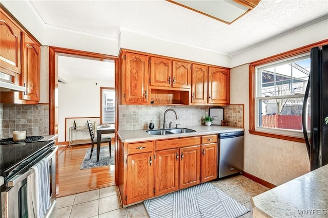 kitchen with brown cabinetry, light countertops, appliances with stainless steel finishes, light tile patterned flooring, and a sink