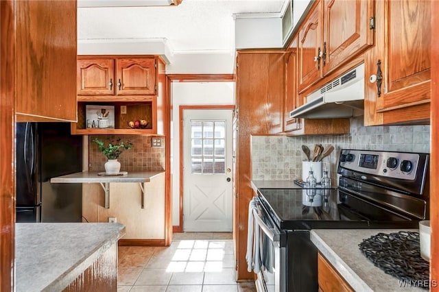 kitchen featuring under cabinet range hood, freestanding refrigerator, stainless steel range with electric cooktop, brown cabinetry, and decorative backsplash