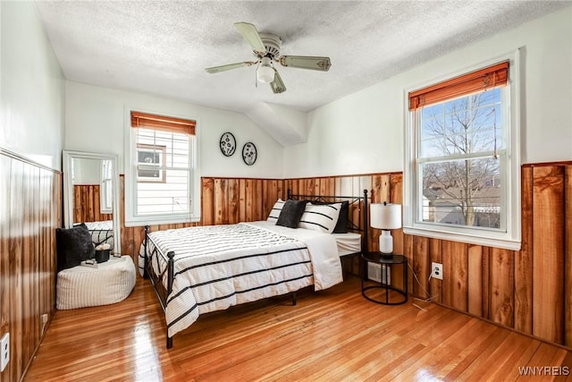 bedroom with hardwood / wood-style floors, multiple windows, a wainscoted wall, and wood walls