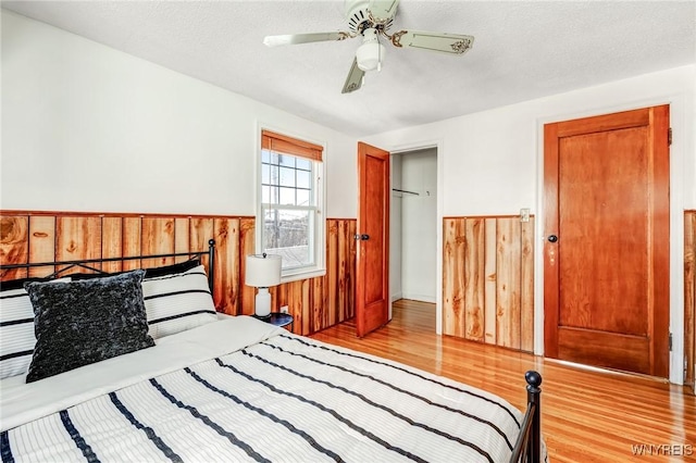 bedroom with a wainscoted wall, a ceiling fan, a textured ceiling, wood finished floors, and wood walls