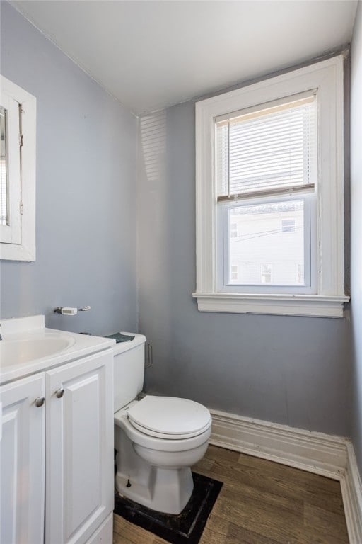 half bath featuring toilet, vanity, baseboards, and wood finished floors