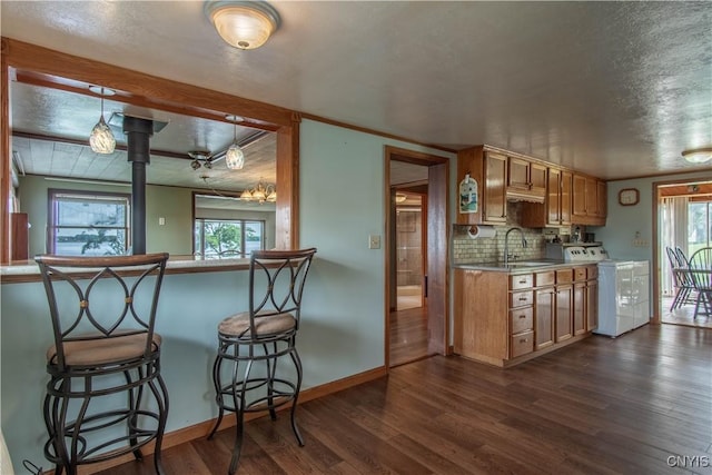 kitchen featuring baseboards, dark wood finished floors, decorative backsplash, washer / clothes dryer, and a sink