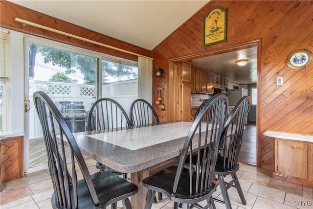 dining space with a wealth of natural light, light tile patterned floors, wood walls, and vaulted ceiling