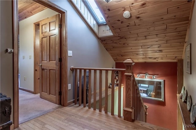 corridor with an upstairs landing, hardwood / wood-style floors, a skylight, wooden ceiling, and baseboards