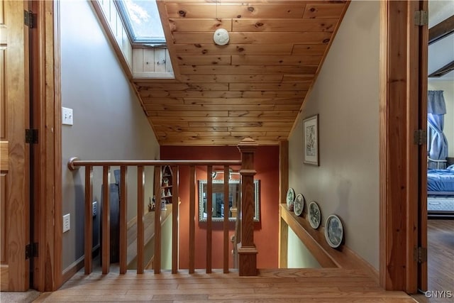 interior space with wood finished floors, vaulted ceiling with skylight, an upstairs landing, and wood ceiling