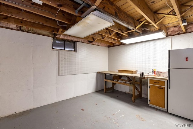 unfinished basement featuring a workshop area and freestanding refrigerator