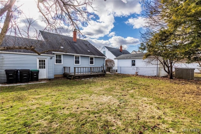 rear view of house with a lawn, a chimney, a deck, and fence