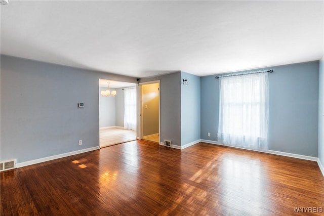 unfurnished room featuring visible vents, baseboards, a notable chandelier, and wood finished floors