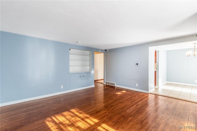 spare room featuring built in features, visible vents, an inviting chandelier, and wood finished floors