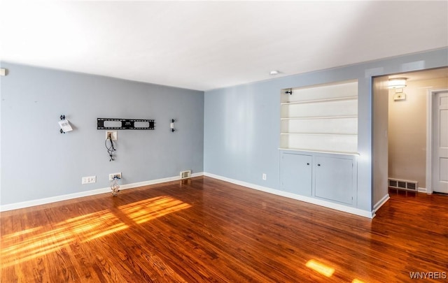 unfurnished living room featuring visible vents, built in features, baseboards, and wood finished floors