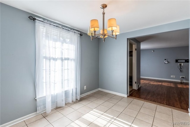 empty room with light tile patterned floors, baseboards, and a chandelier