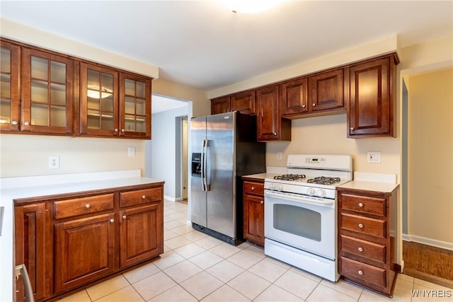 kitchen with white gas stove, stainless steel fridge, glass insert cabinets, and light countertops