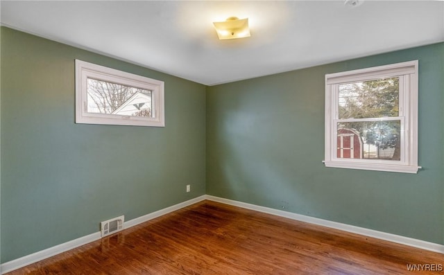 spare room with visible vents, plenty of natural light, baseboards, and wood finished floors