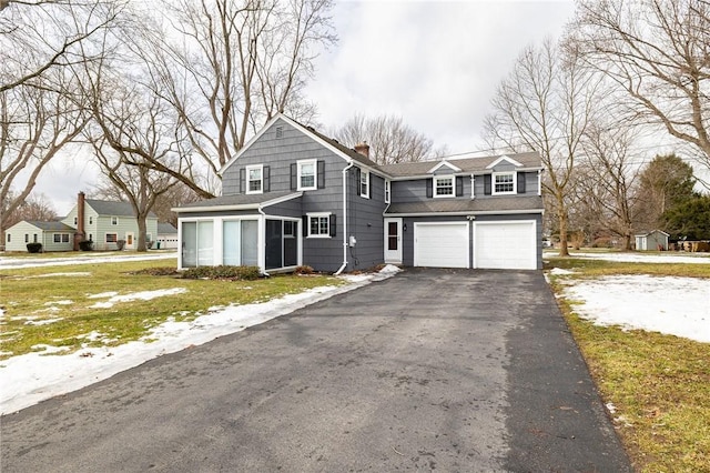 view of front of home featuring aphalt driveway, a chimney, a garage, and a sunroom