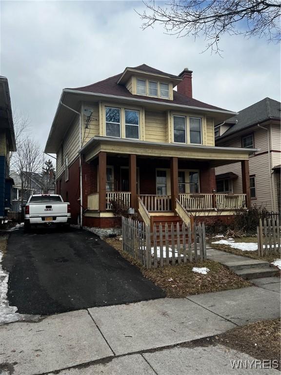 traditional style home featuring a porch, aphalt driveway, and a chimney