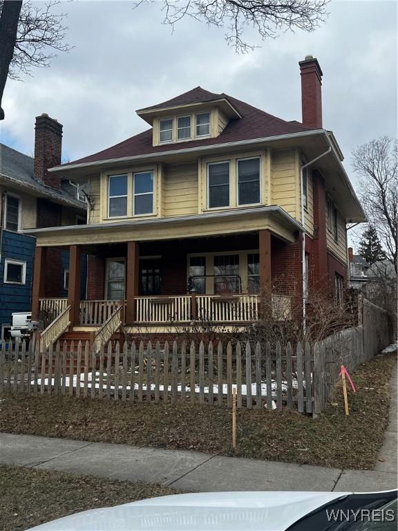 american foursquare style home featuring a fenced front yard, covered porch, and a chimney