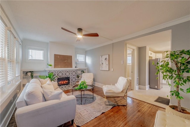 living area featuring a fireplace, crown molding, baseboards, and wood finished floors