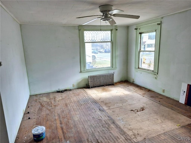 empty room with hardwood / wood-style floors, radiator, a ceiling fan, and ornamental molding