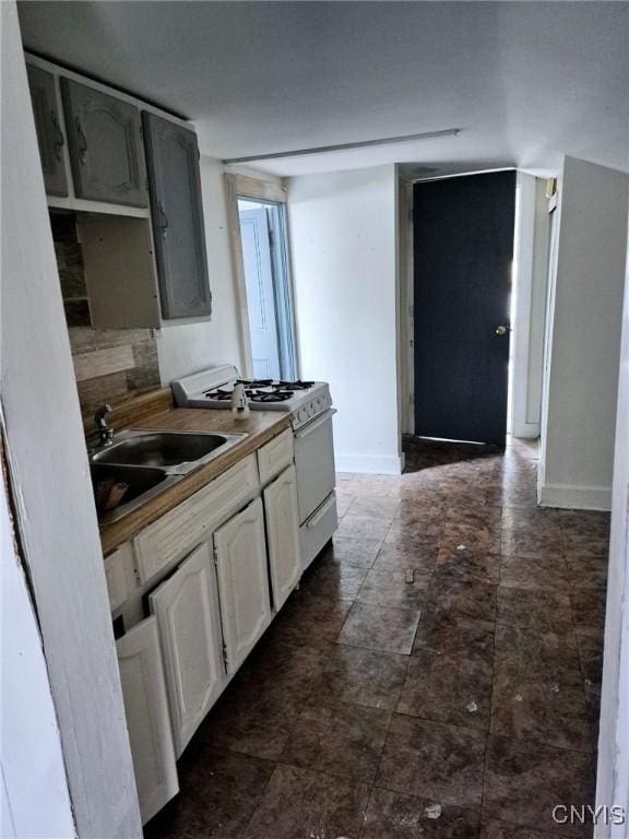 kitchen with a sink, baseboards, white gas range, and white cabinetry