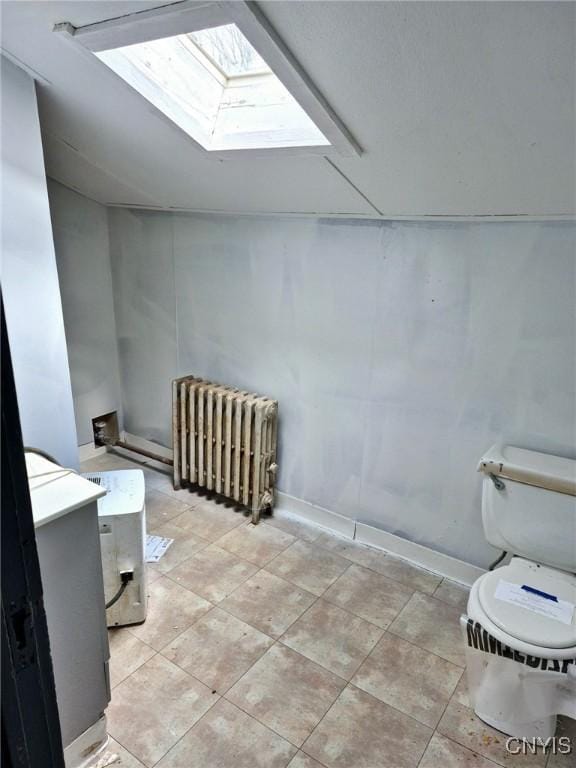 bathroom featuring toilet, lofted ceiling with skylight, radiator heating unit, and baseboards