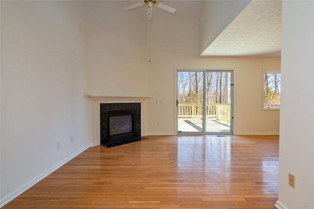 unfurnished living room with light wood-style flooring, a towering ceiling, a fireplace, baseboards, and ceiling fan