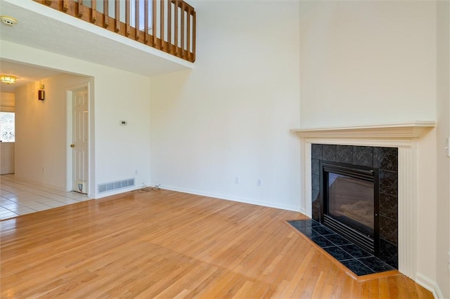 unfurnished living room with wood finished floors, visible vents, baseboards, a fireplace, and a towering ceiling